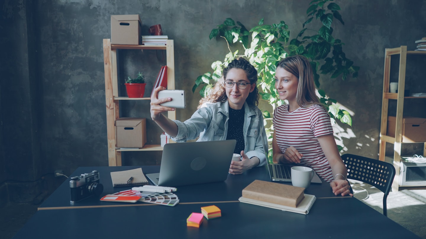 Two women take a selfie at a desk