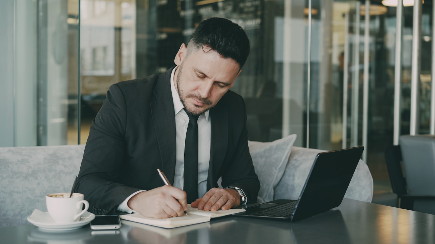 Man in suit writing in notebook at table