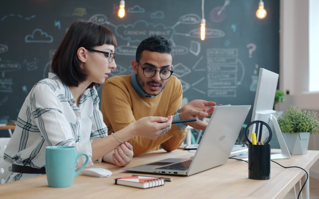 Two colleagues collaborating on a laptop at a desk