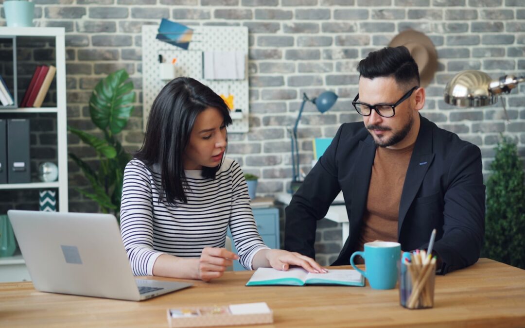 a man and a woman sitting at a table looking at a laptop