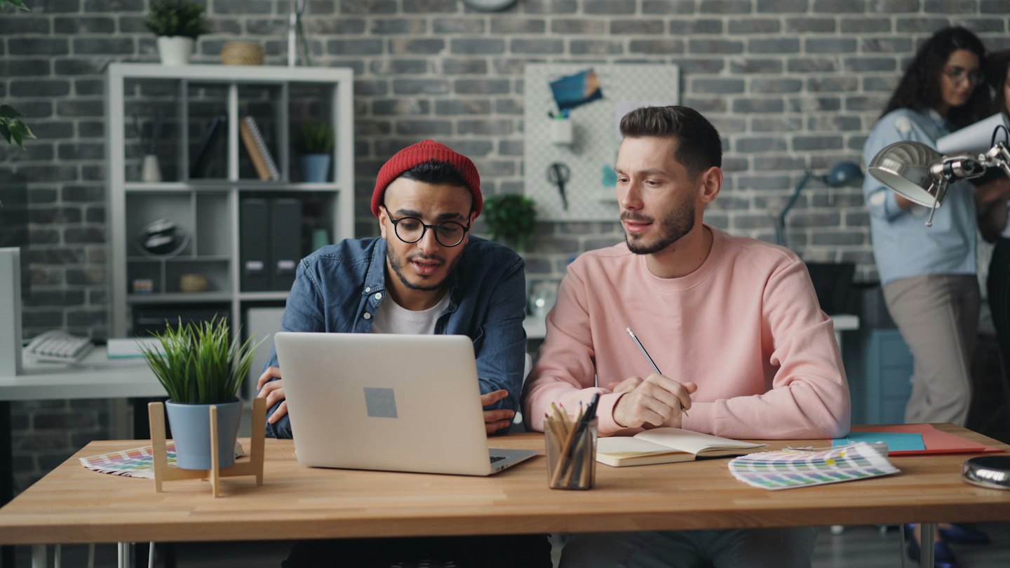 two men sitting at a table working on a laptop