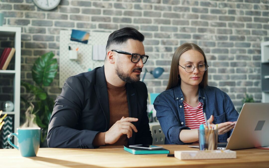 a man and a woman sitting at a table looking at a laptop