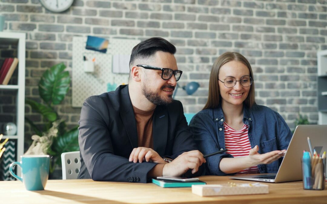 a man and a woman sitting at a table looking at a laptop